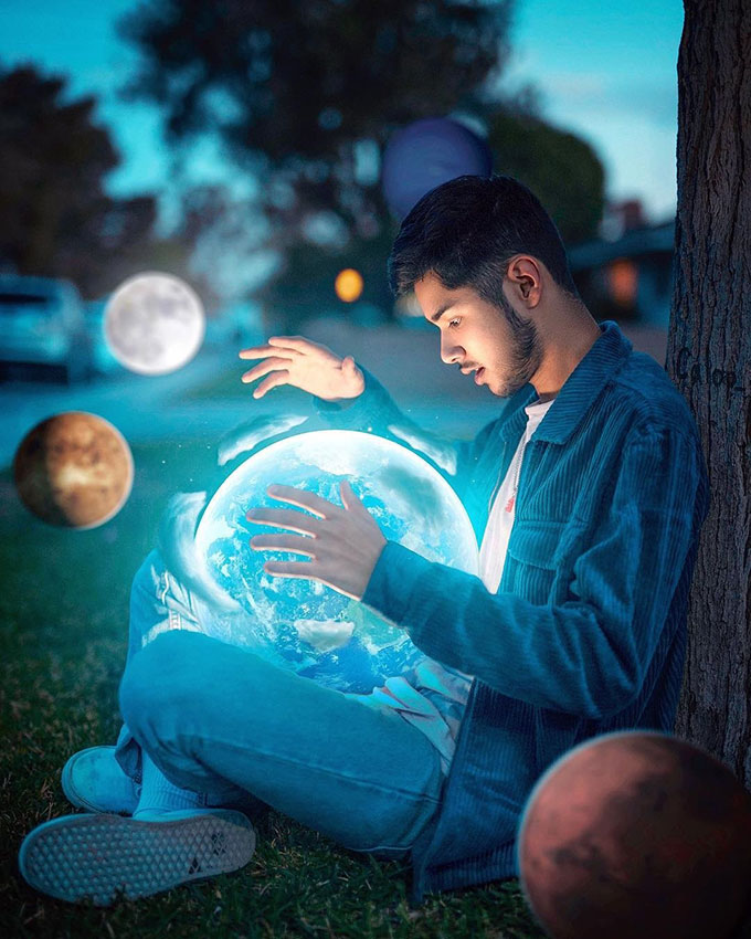 Man sitting with small glowing earth in his lap with small planets around him